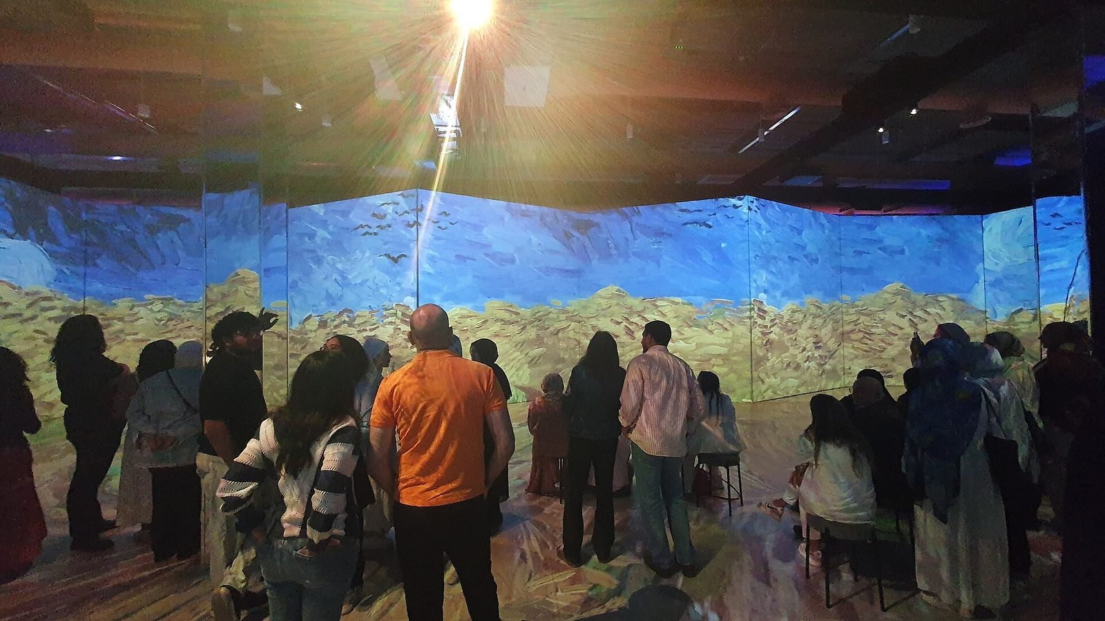 Visitors inside an immersive room with paintings projected on every wall