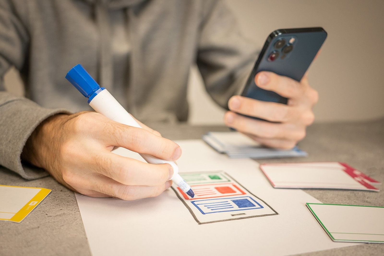A designer sketching interface ideas on paper next to a phone